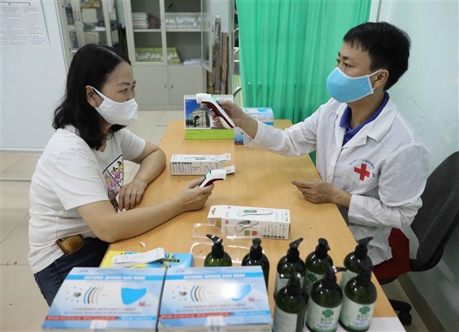  Trong ảnh: Nhân viên y tế Trường THPT Nguyễn Gia Thiều, quận Long Biên hướng dẫn giáo viên sử dụng thiết bị đo thân nhiệt đúng cách. Ảnh: Thanh Tùng - TTXVN   